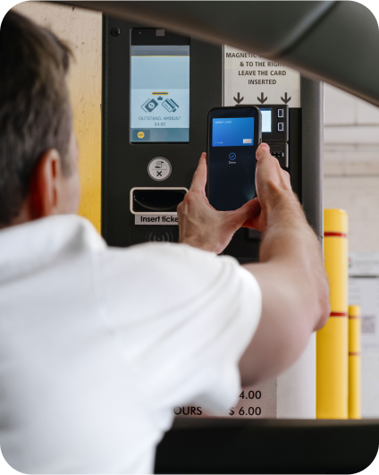 Řidič platí parkovné pomocí mobilního telefonu u parkovacího automatu.