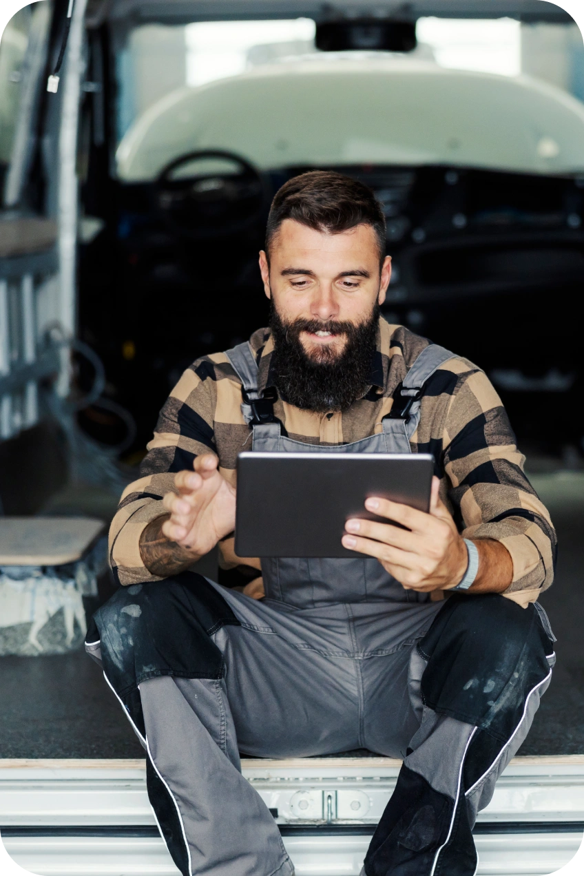 Automechanik sedí v dílně a používá tablet.